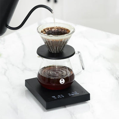 Coffee brewing process with a kettle pouring water into a coffee filter on a digital scale.