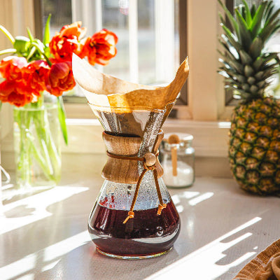 Chemex coffee maker with coffee on a kitchen counter with flowers and a pineapple in the background