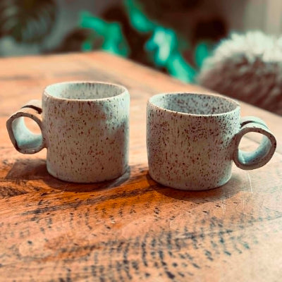 Two ceramic mugs with speckled glaze on a wooden surface.