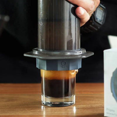 Person using an AeroPress to make coffee on a wooden surface