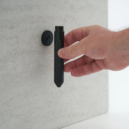 A hand holding a black cylindrical wall-mounted fixture against a light gray textured wall.