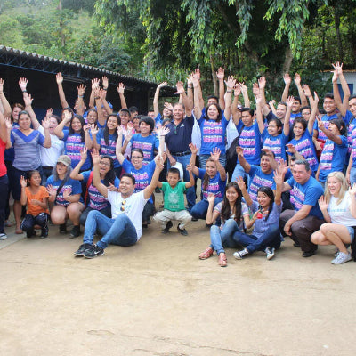 Group of people posing together outdoors with raised hands, wearing matching shirts.
