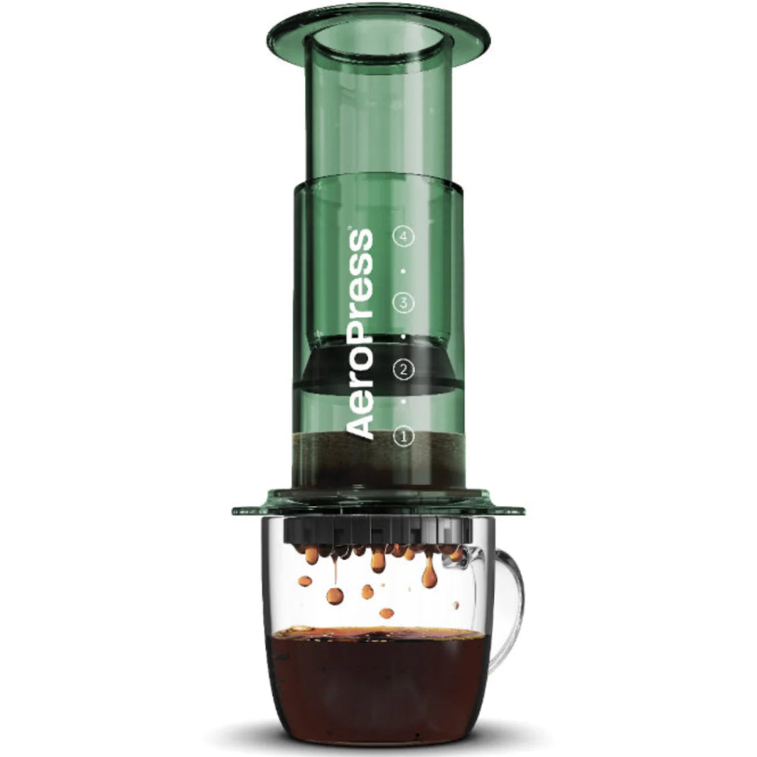 Green AeroPress coffee maker with coffee dripping into a glass mug on a white background