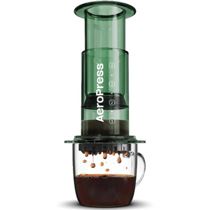 Green AeroPress coffee maker with coffee dripping into a glass mug on a white background