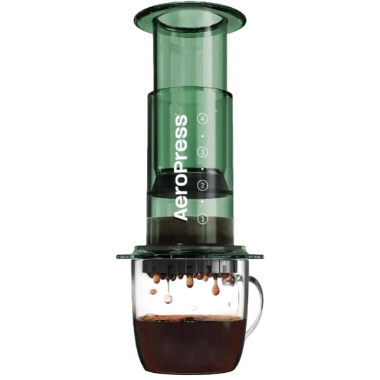 Green AeroPress coffee maker with coffee dripping into a glass mug on a white background