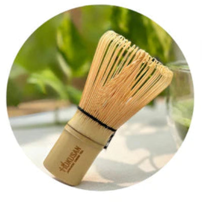 Bamboo whisk with wooden handle and green leaves in the background
