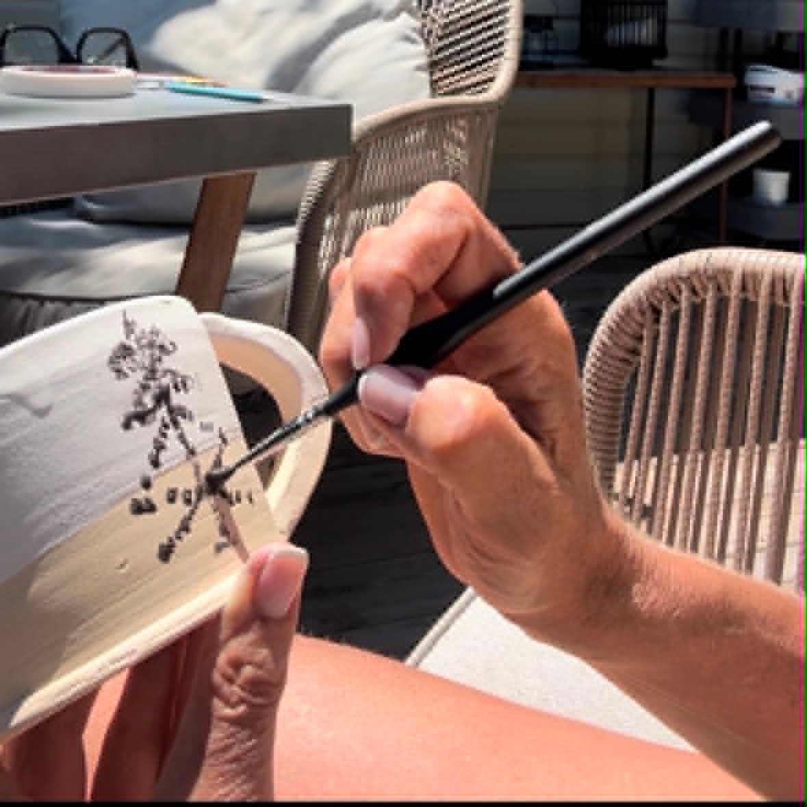 Person holding a brush and painting on a small canvas outdoors.