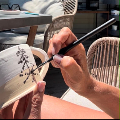 Person holding a brush and painting on a small canvas outdoors.