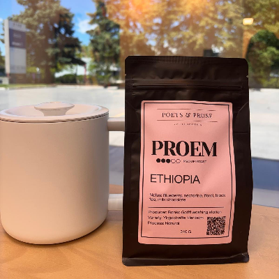 Coffee bag labeled 'Proem Ethiopia' next to a white mug on a table outdoors.