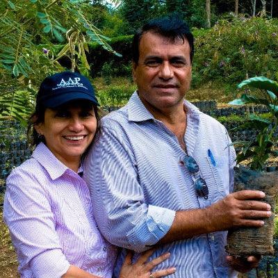 Two people standing together in a natural setting, one holding a plant.