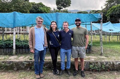 Four people standing together in front of a blue tarp and greenery