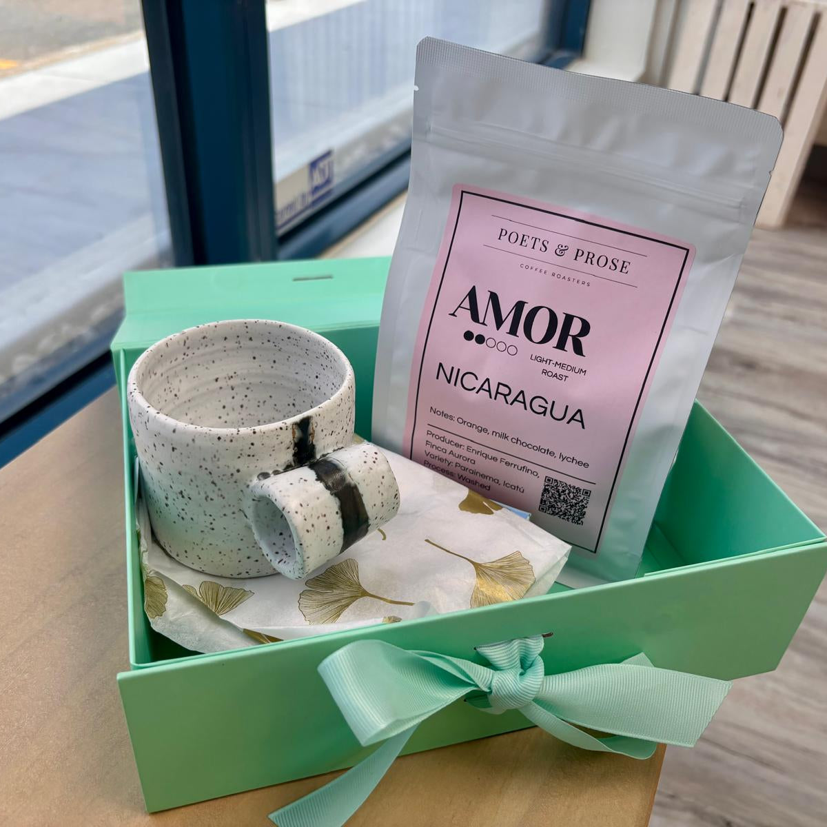 Handmade coffee mug and 'Amor Nicaragua' coffee package in a green box on a table.