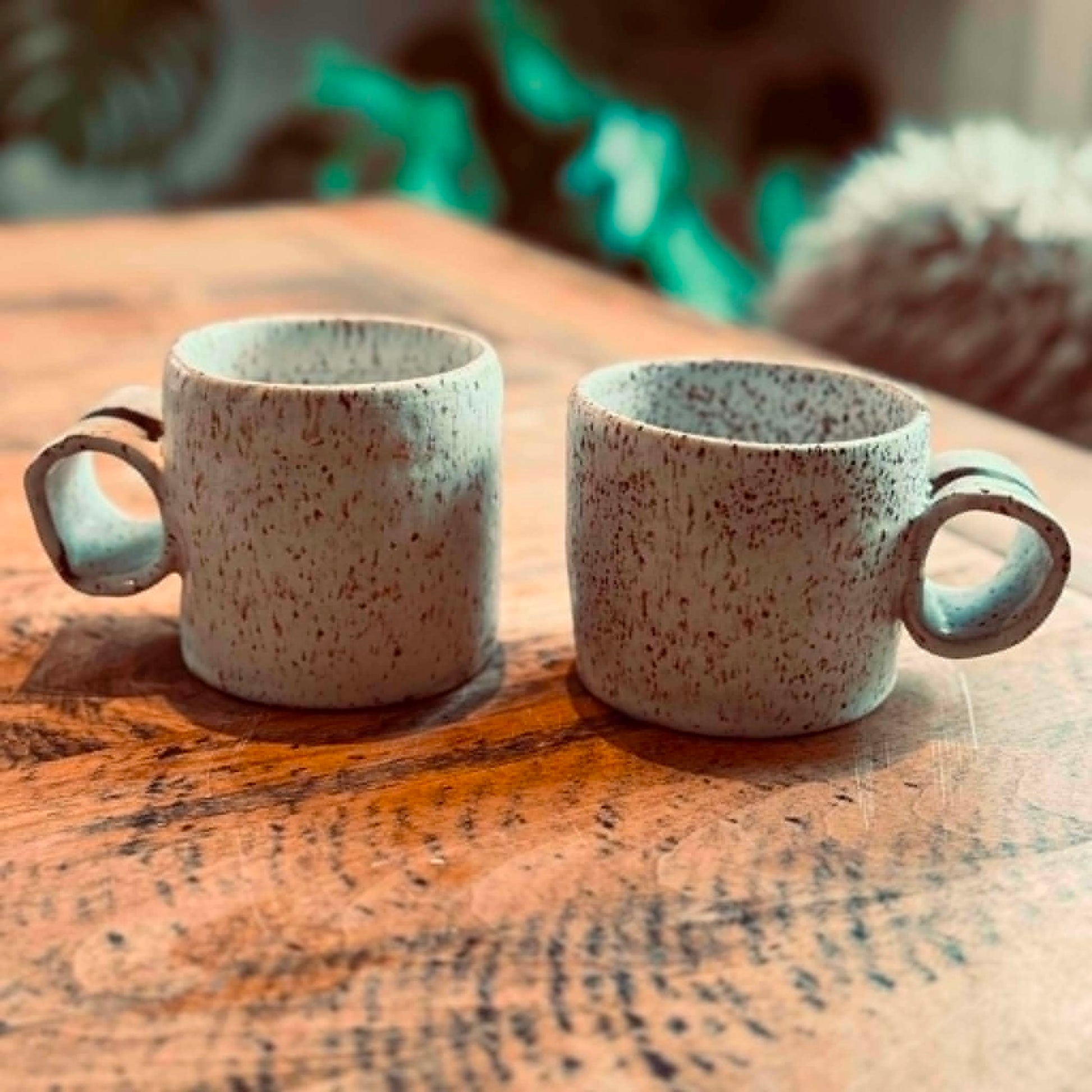 Two ceramic mugs with speckled glaze on a wooden surface.