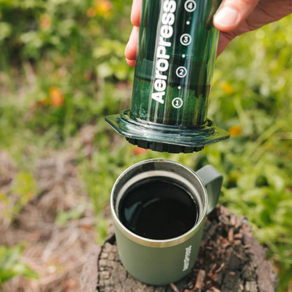 A person using an Aeropress to make coffee outdoors on a tree stump.