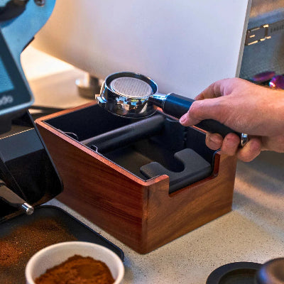 Person using a coffee tamping device on a coffee machine with a wooden base.