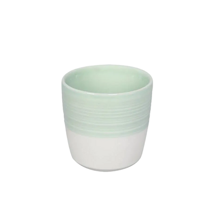 A small ceramic cup with a two-tone design, featuring a pale mint green upper half with horizontal ridges and a white lower half, set against a plain white background.