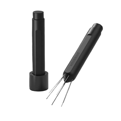 A black cylindrical cleaning tool with four thin metal prongs, shown alongside its matching black charging base on a dark gray background.