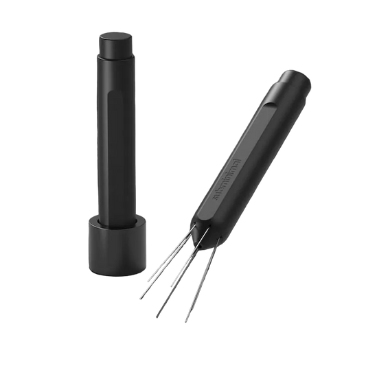 A black cylindrical cleaning tool with four thin metal prongs, shown alongside its matching black charging base on a dark gray background.
