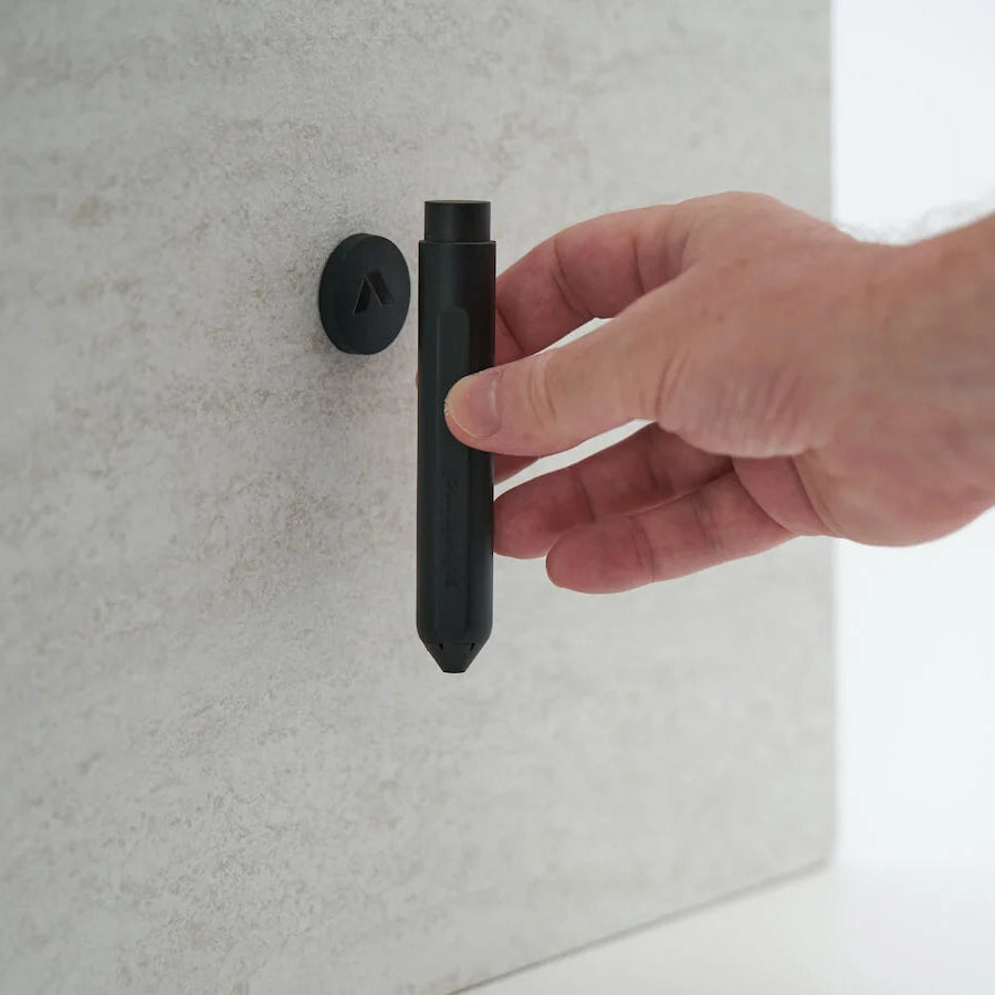 A hand holding a black cylindrical wall-mounted fixture against a light gray textured wall.