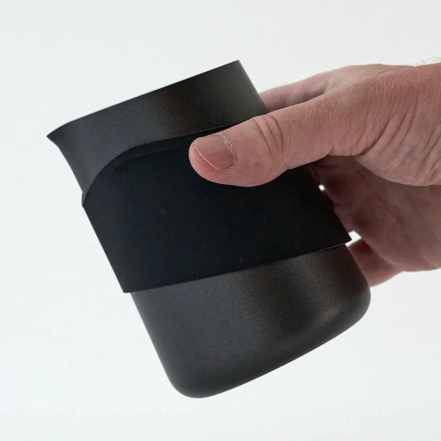 A hand holding a matte black insulated cup or tumbler with a matching black sleeve around the middle, photographed against a clean white background.