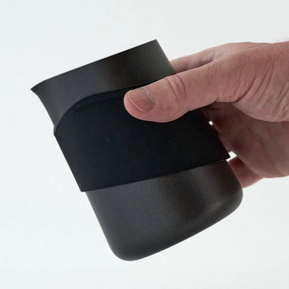 A hand holding a matte black insulated cup or tumbler with a matching black sleeve around the middle, photographed against a clean white background.