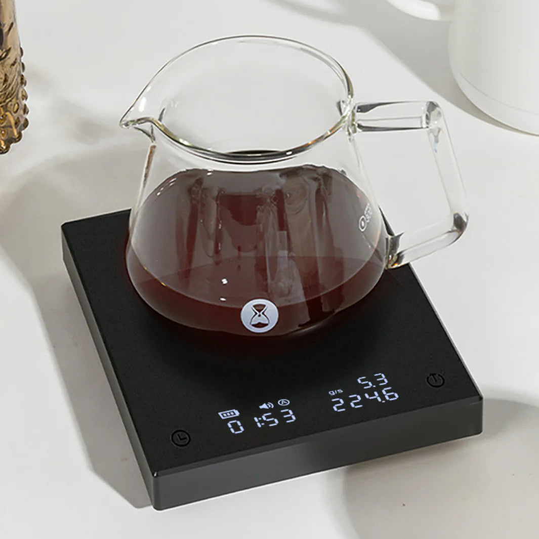 Clear glass coffee pot with dark liquid on a digital scale against a white background