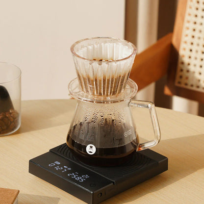Coffee brewing setup with a glass carafe on a digital scale on a wooden table.